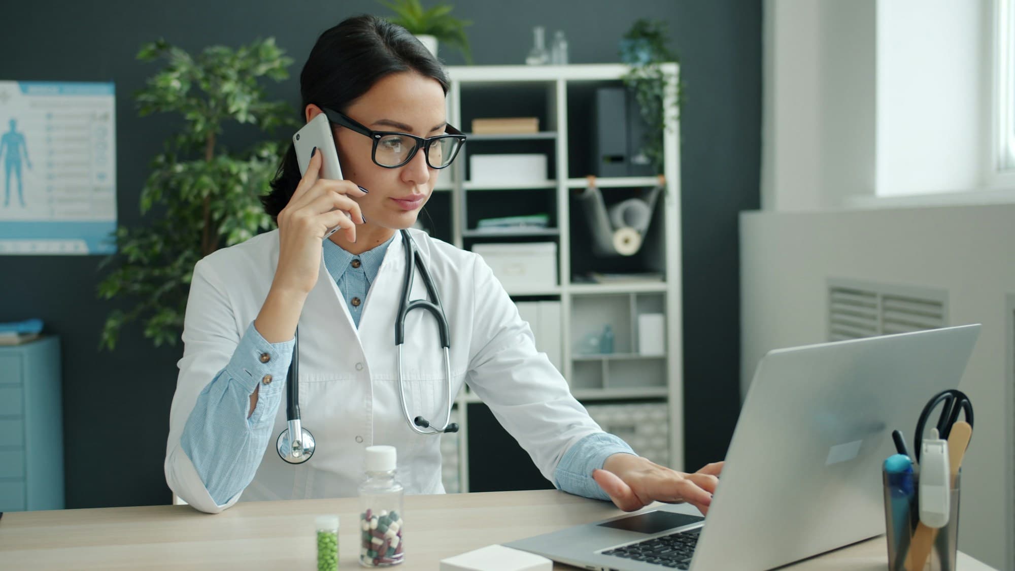 A doctor on the phone while working at a laptop